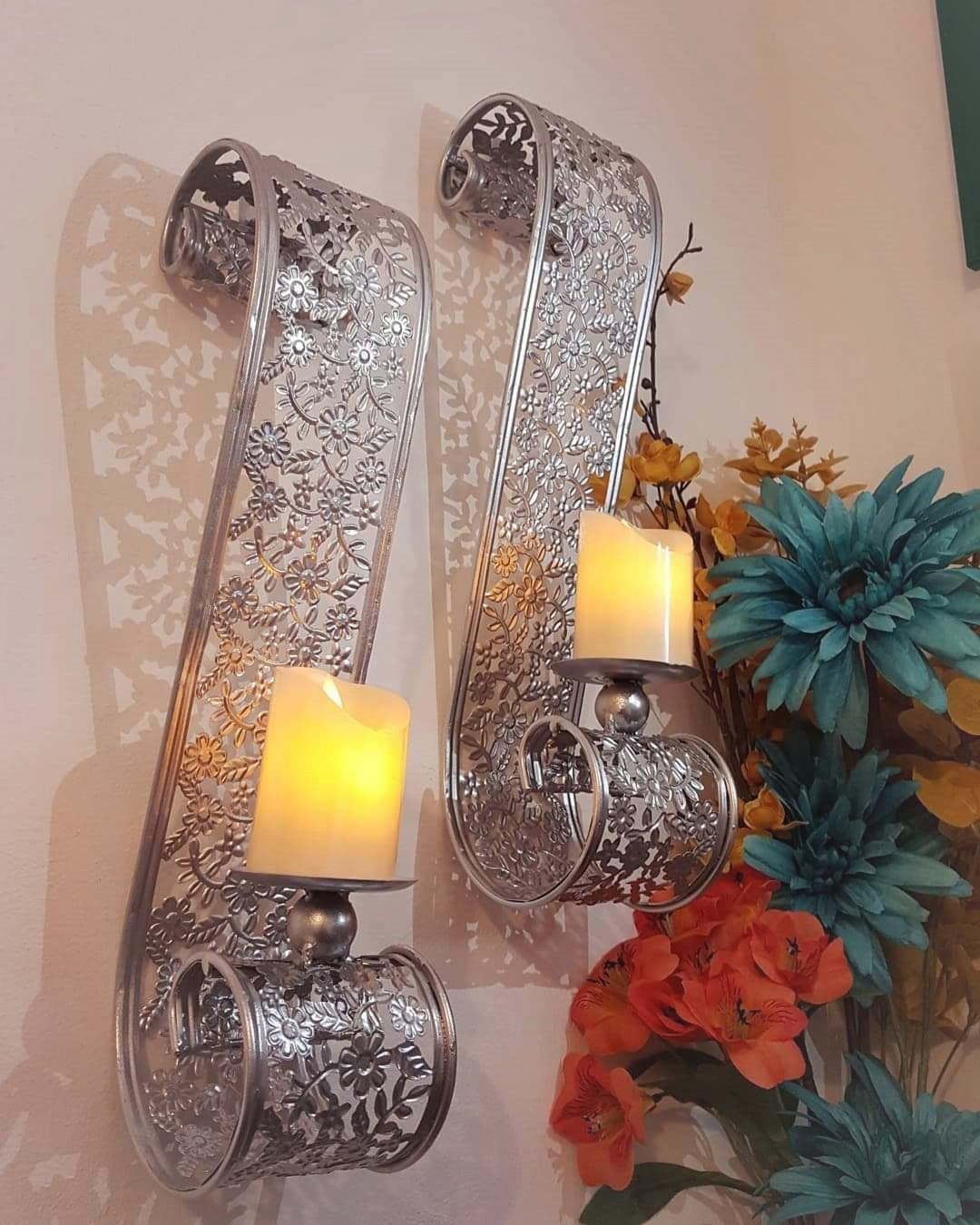 Pair of silver metal scroll wall candle sconces with lit candles beside flowers